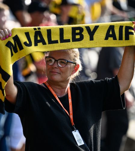 Kvinnlig dupporter håller upp halsduk med texten "Mjällby IF" under en match