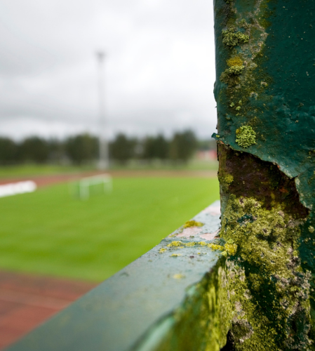 Stolpe i förgrund med suddig fotbollsplan bakom