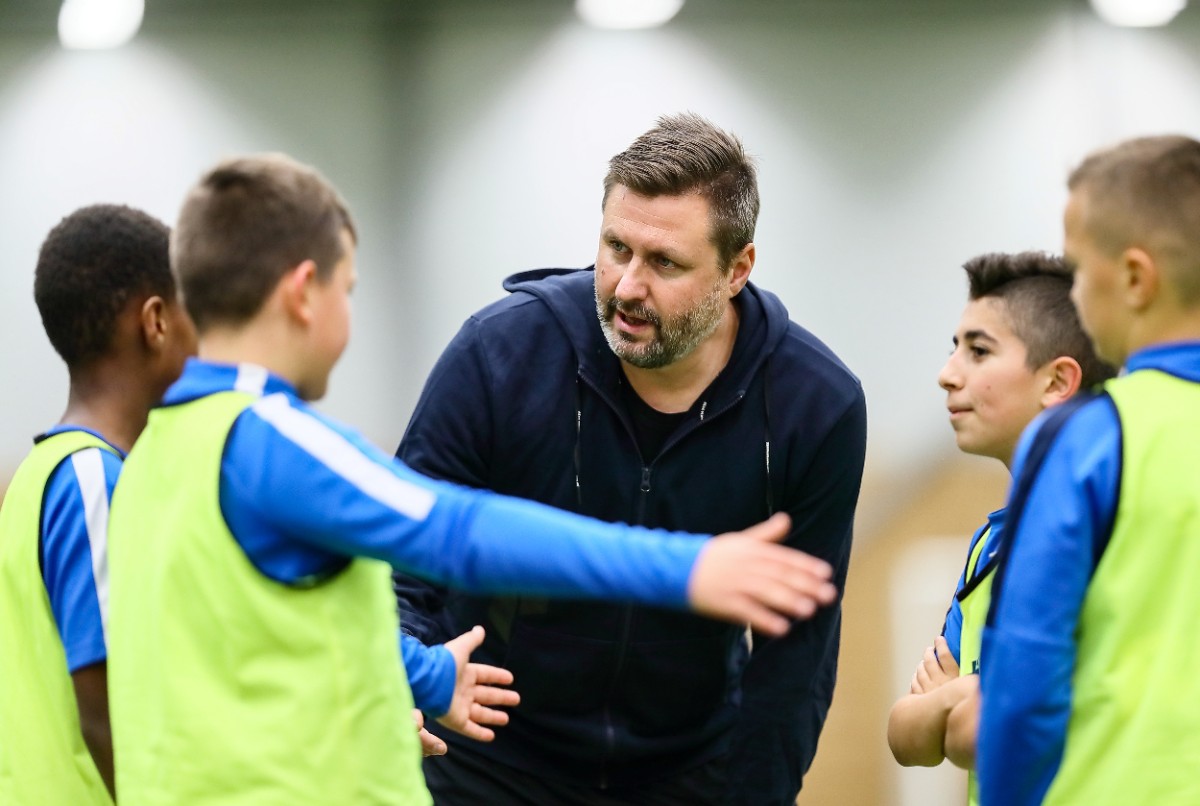 Manlig tränare pratar med barn som är samlade i en ring 