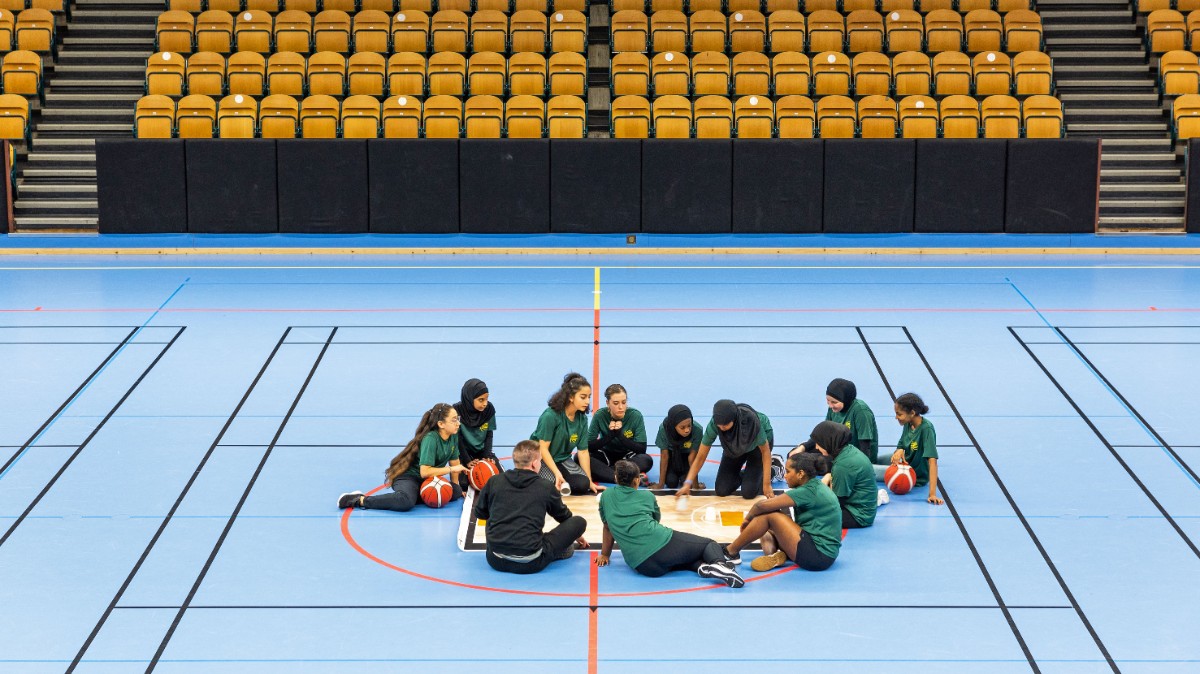 Ungdomar sitter i mittcirkeln på en handbollsplan och pratar