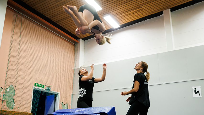 Tjej gör gymnastikvolt och 2 ledare står beredda.