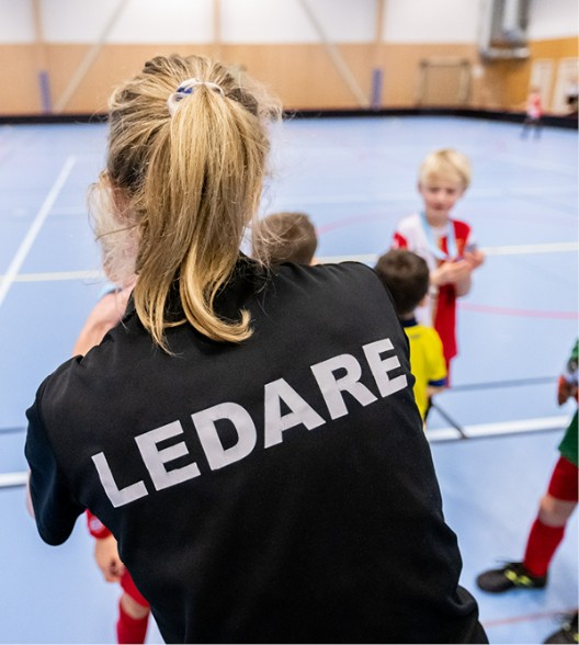 Kvinnlig ledare som står med barn i idrottshall.
