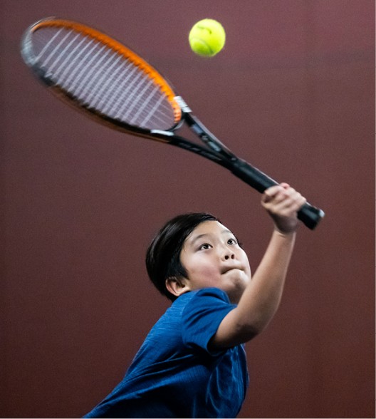 Pojke som spelar tennis och tar emot en hög boll