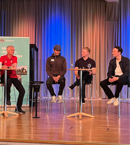 Personer i panelsamtal sitter på stolar på scenen.