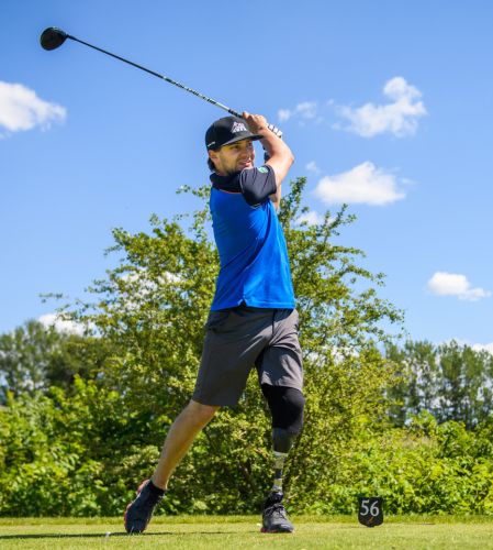 Man svingar en golfklubba på en golfbana i solen. 