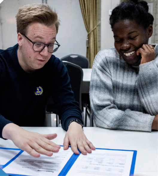 Bild på två personer som sitter och diskuterar vid ett bord.
