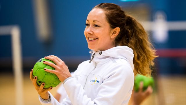 Kvinna ler och håller en handboll i båda händerna