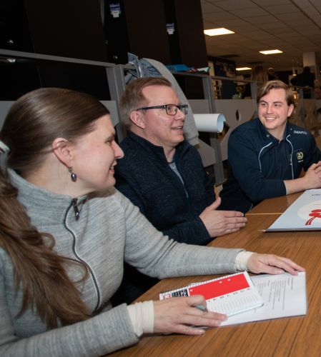 Tre personer sitter vid ett skrivbord och diskuterar